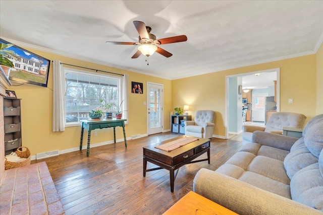 living room with a ceiling fan, visible vents, baseboards, ornamental molding, and wood-type flooring