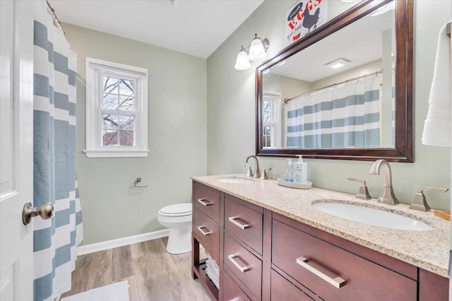 full bathroom with double vanity, a sink, toilet, and wood finished floors