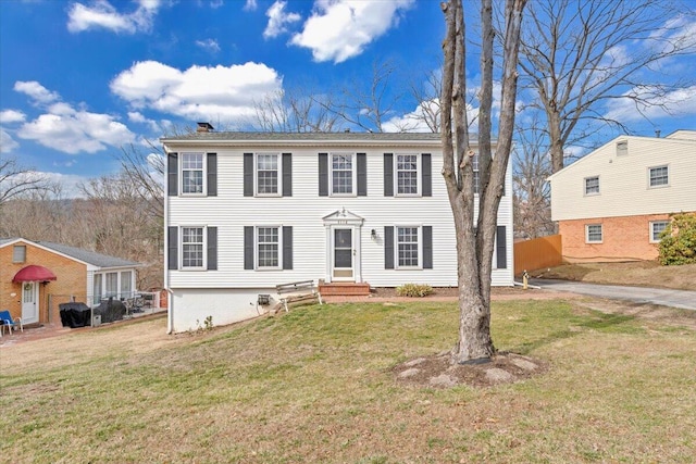 colonial home with entry steps, a chimney, and a front yard