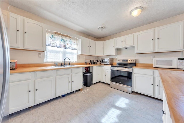 kitchen featuring appliances with stainless steel finishes, butcher block countertops, a sink, and white cabinetry