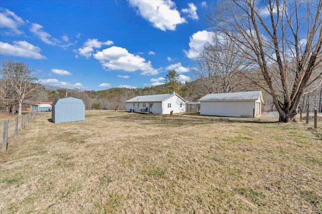 view of yard with a storage shed, a rural view, fence, and an outdoor structure