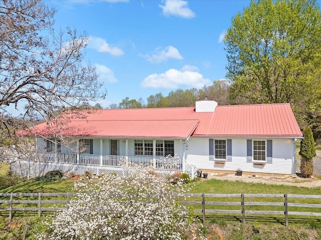 single story home with a chimney, covered porch, metal roof, fence, and a front yard