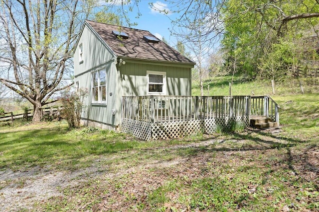 rear view of property featuring a lawn, a wooden deck, and a shingled roof