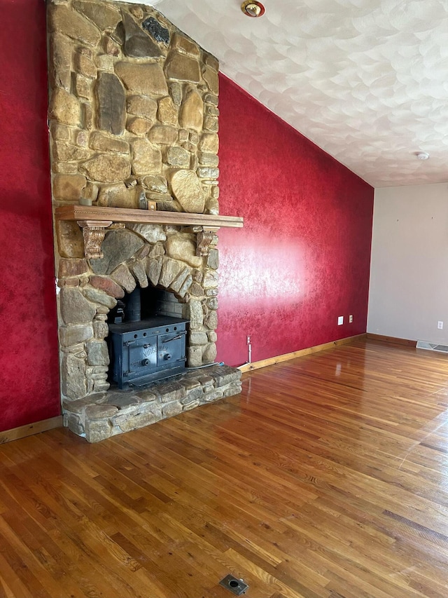 unfurnished living room featuring a wood stove, baseboards, and wood finished floors