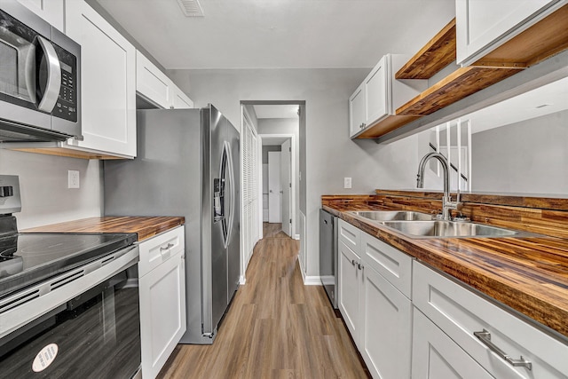 kitchen featuring butcher block countertops, a sink, open shelves, stainless steel appliances, and light wood finished floors