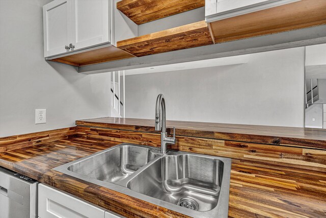 kitchen with a sink, butcher block countertops, dishwasher, and white cabinetry