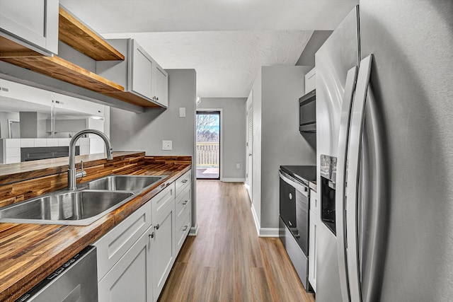 kitchen featuring a sink, appliances with stainless steel finishes, wood finished floors, wood counters, and open shelves