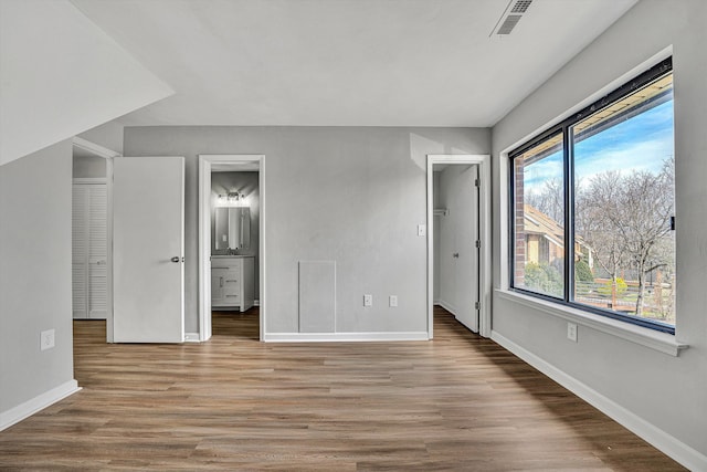 unfurnished bedroom with visible vents, a walk in closet, light wood-style flooring, ensuite bathroom, and baseboards