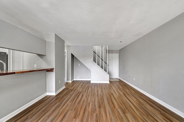 unfurnished living room featuring stairway, baseboards, and wood finished floors