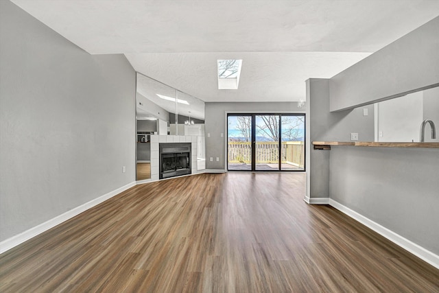 unfurnished living room featuring lofted ceiling with skylight, baseboards, wood finished floors, and a fireplace