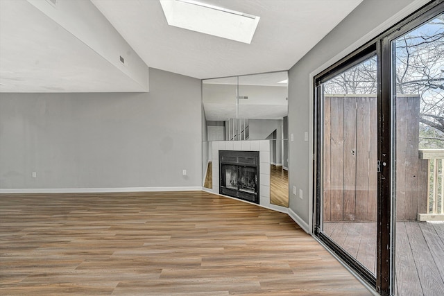 unfurnished living room with light wood finished floors, a fireplace, a skylight, and baseboards