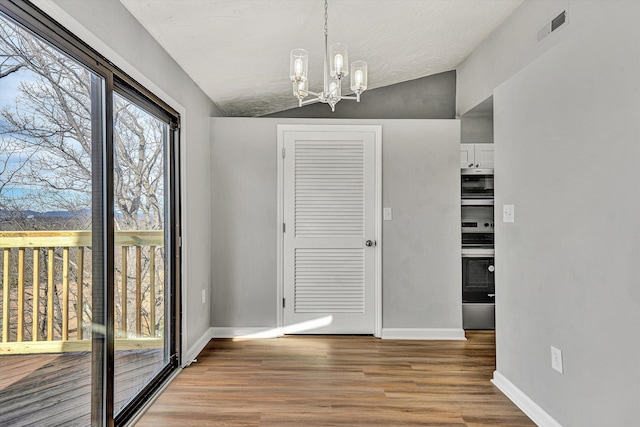 unfurnished dining area featuring visible vents, lofted ceiling, baseboards, and wood finished floors