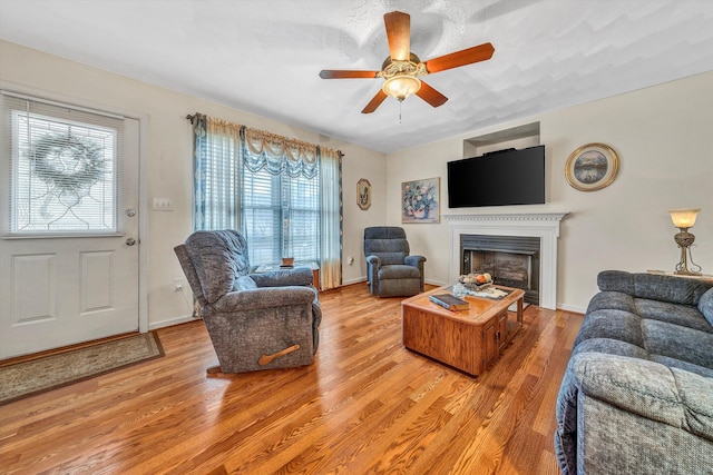 living area with a ceiling fan, a fireplace, light wood-style flooring, and baseboards