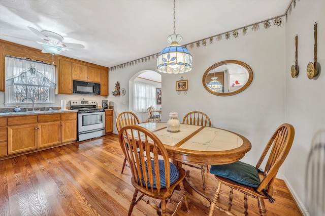 dining room with arched walkways, ceiling fan, light wood-type flooring, and baseboards