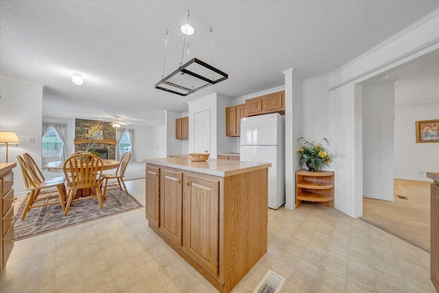 kitchen featuring light countertops, freestanding refrigerator, a kitchen island, visible vents, and light floors