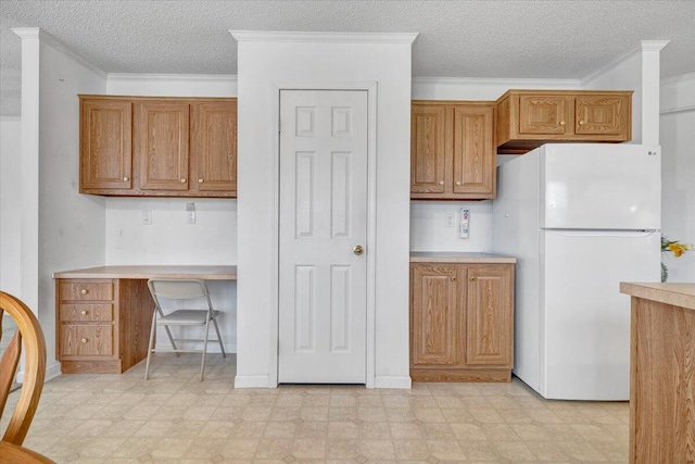 kitchen featuring built in desk, freestanding refrigerator, light floors, and brown cabinets