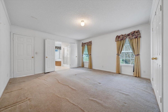 unfurnished bedroom featuring ensuite bathroom, multiple windows, carpet flooring, and a textured ceiling