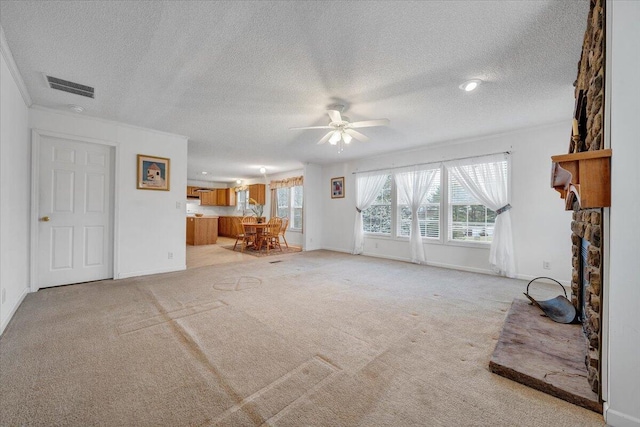 unfurnished living room with ceiling fan, a fireplace, a textured ceiling, light colored carpet, and visible vents