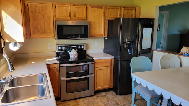 kitchen featuring a sink, light countertops, appliances with stainless steel finishes, stone finish flooring, and brown cabinets