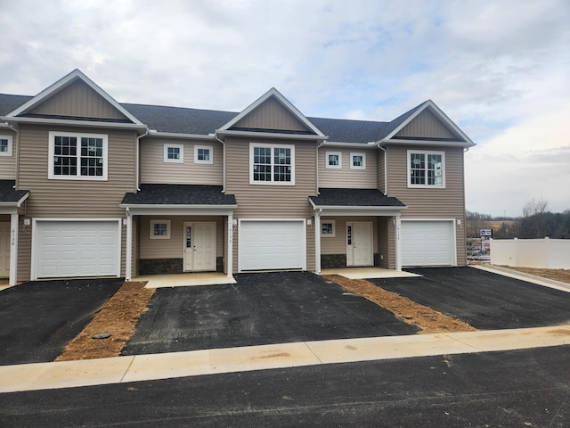 townhome / multi-family property featuring a shingled roof, driveway, and an attached garage