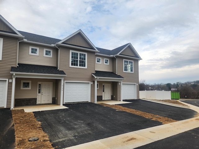 multi unit property with board and batten siding, roof with shingles, driveway, and an attached garage