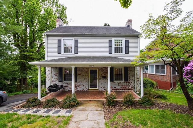 view of front facade featuring covered porch, brick siding, and a chimney