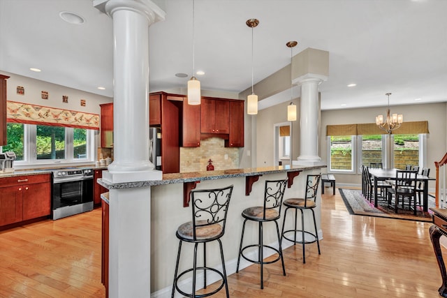 kitchen featuring appliances with stainless steel finishes, a kitchen bar, decorative columns, and light wood-style floors