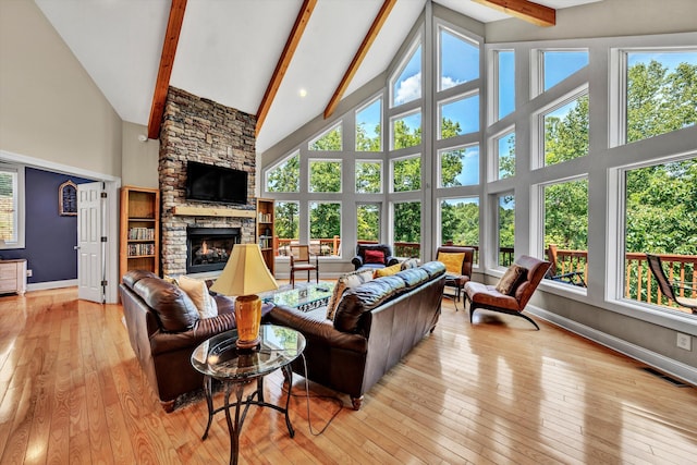 living area featuring a fireplace, beamed ceiling, light wood-style flooring, high vaulted ceiling, and plenty of natural light