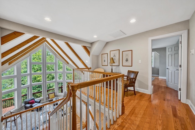 corridor with lofted ceiling, visible vents, baseboards, an upstairs landing, and light wood-style floors