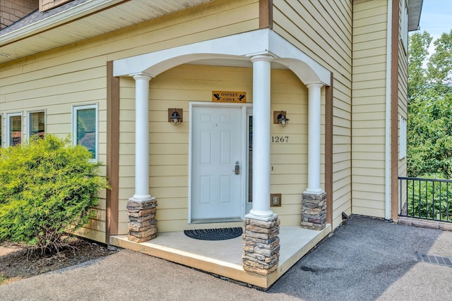 view of exterior entry with stone siding, a shingled roof, visible vents, and covered porch