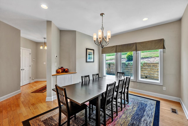 dining area featuring light wood finished floors, baseboards, visible vents, and a notable chandelier