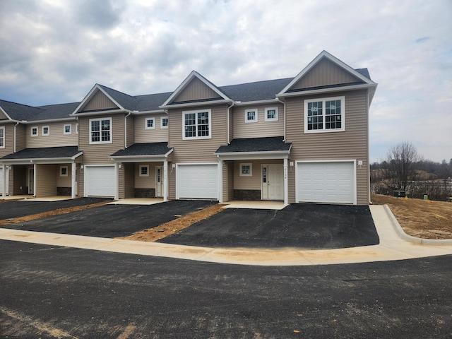 multi unit property with a garage, driveway, and roof with shingles