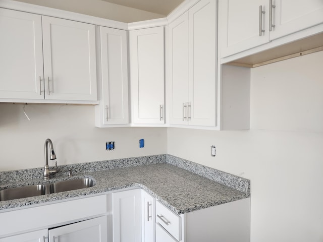 kitchen featuring light stone countertops, white cabinetry, and a sink