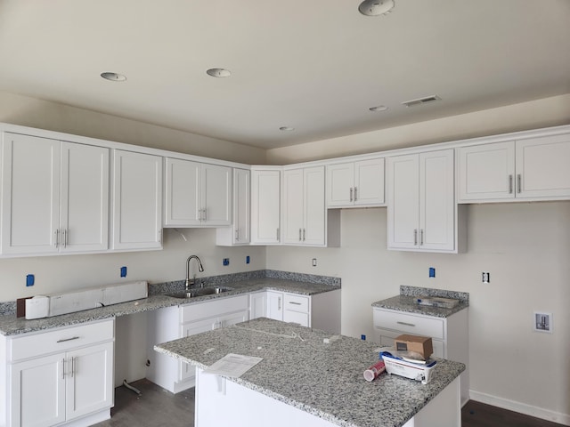 kitchen featuring stone counters, a center island, white cabinets, and a sink