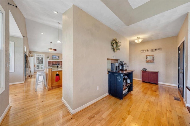 corridor with light wood-type flooring, visible vents, baseboards, and lofted ceiling