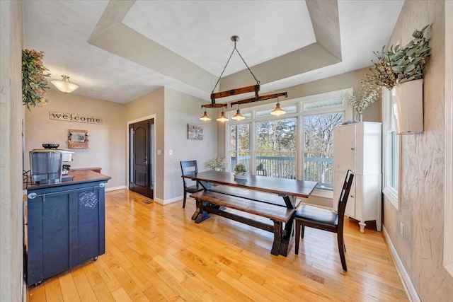 dining room featuring light wood finished floors, baseboards, and a tray ceiling