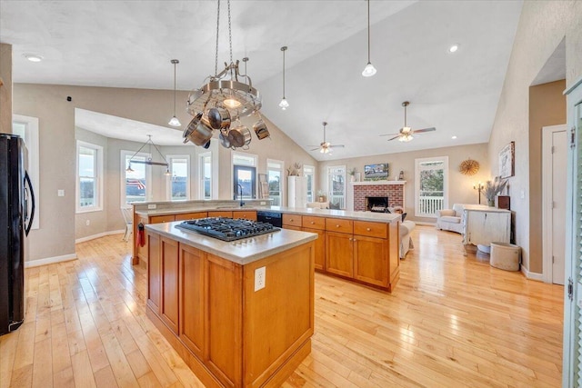 kitchen with a sink, open floor plan, black appliances, light wood finished floors, and a large island with sink