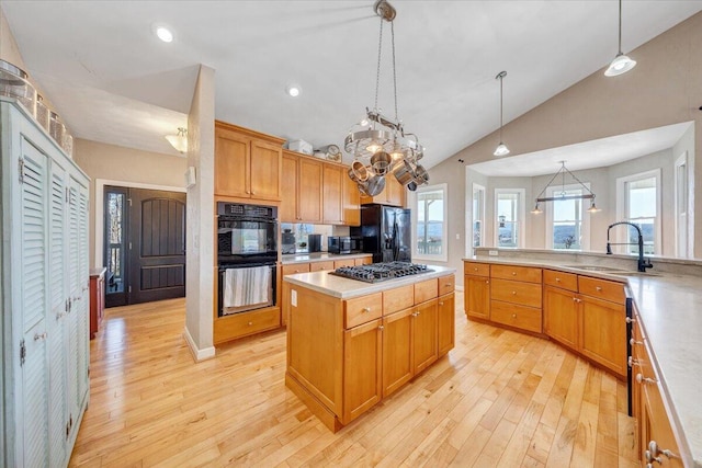 kitchen featuring light countertops, vaulted ceiling, a sink, light wood-type flooring, and black appliances