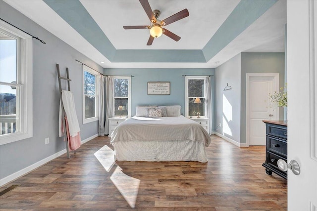 bedroom with a tray ceiling, ceiling fan, baseboards, and wood finished floors