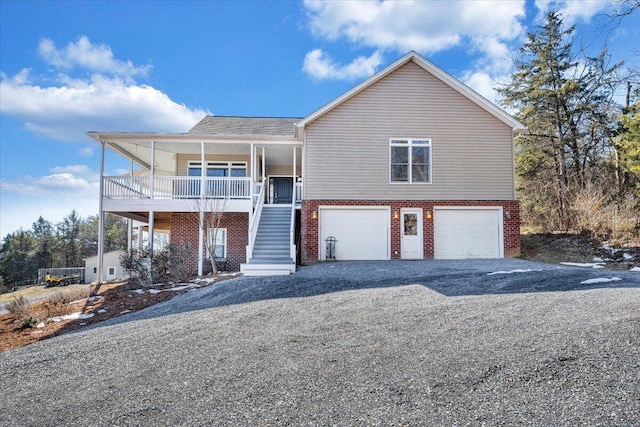 view of front facade featuring covered porch, a garage, brick siding, stairs, and gravel driveway