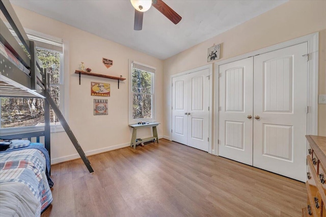 bedroom featuring light wood finished floors, two closets, a ceiling fan, and baseboards