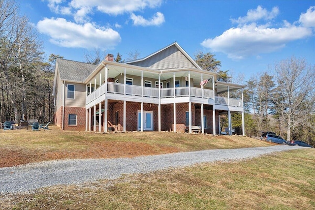 view of front of property featuring a front lawn, a chimney, gravel driveway, and brick siding