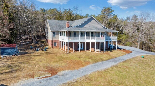 back of house with driveway, brick siding, a chimney, and a yard