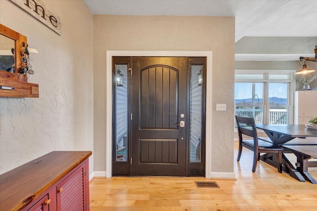 entrance foyer with baseboards, a textured wall, visible vents, and light wood-style floors