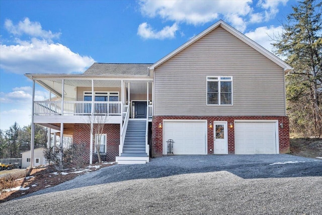 view of front of house featuring brick siding, covered porch, stairway, a garage, and driveway