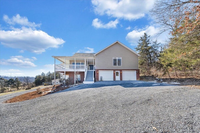 view of front of home featuring brick siding, covered porch, stairway, a garage, and driveway