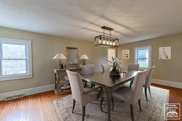 dining area with a textured ceiling, hardwood / wood-style floors, visible vents, and baseboards