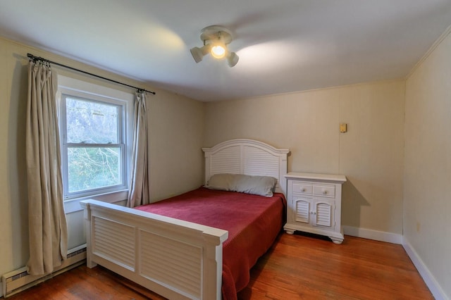 bedroom with a baseboard heating unit, ceiling fan, wood finished floors, and baseboards