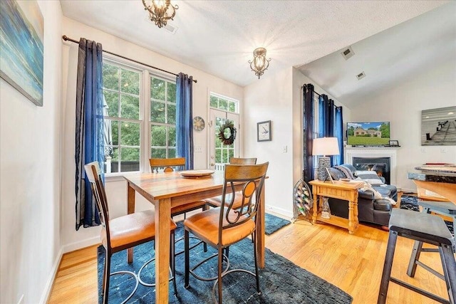 dining room with light wood-type flooring, baseboards, lofted ceiling, and a glass covered fireplace