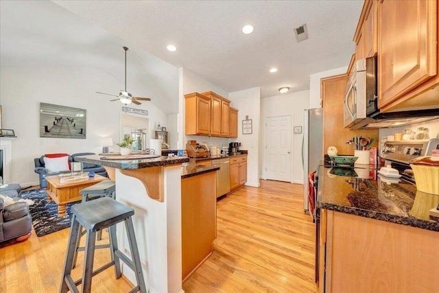 kitchen with a peninsula, a kitchen breakfast bar, open floor plan, appliances with stainless steel finishes, and light wood finished floors